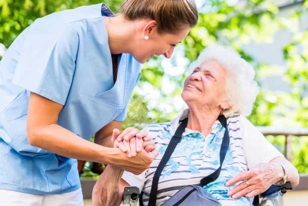 assisted living vs nursing home: Caregiver holding the hand of an elderly woman who is in a wheelchair. difference between assisted living and nursing home