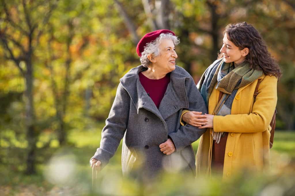 assisted living vs skilled nursing. Caregiver walking outside with a senior woman during the autumn.