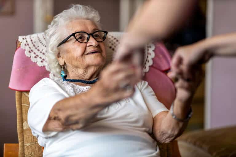 Female home caregiver helping senior woman stand up from a chair at home