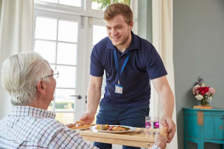 Male caregiver serving dinner to an elderly man at an assisted living facility