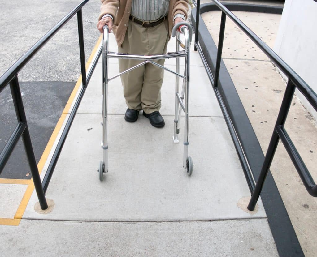 Elderly man walking up a wheelchair ramp with a walker