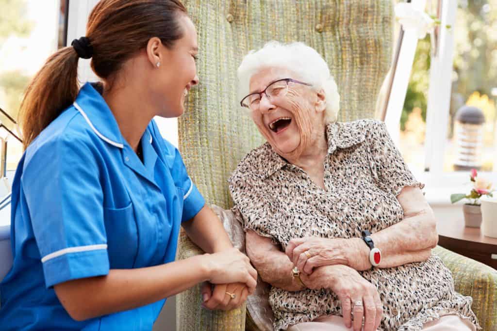 A senior woman sitting and laughing with a nurse