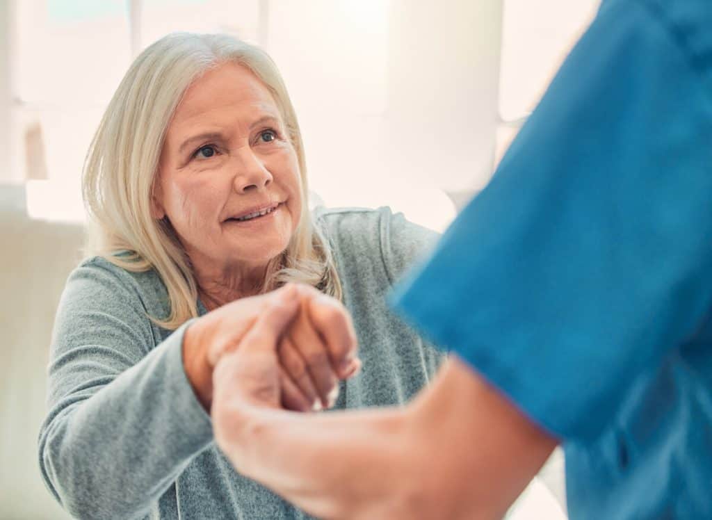 Caregiver in retirement facility helping elderly woman to stand up