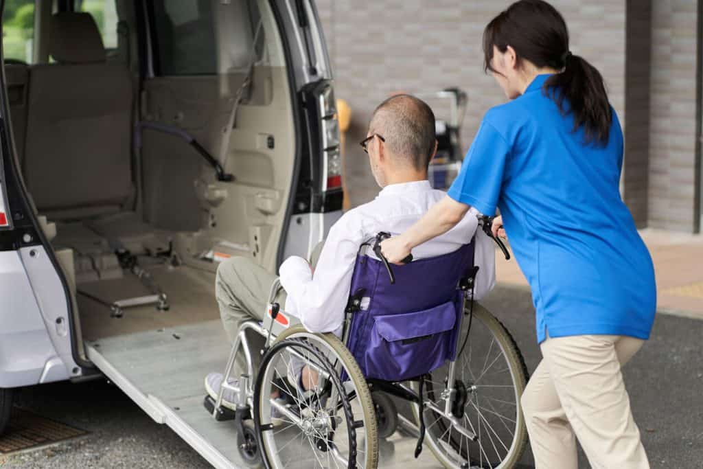 Part time caregiver jobs: Female caregiver putting an elderly man in van