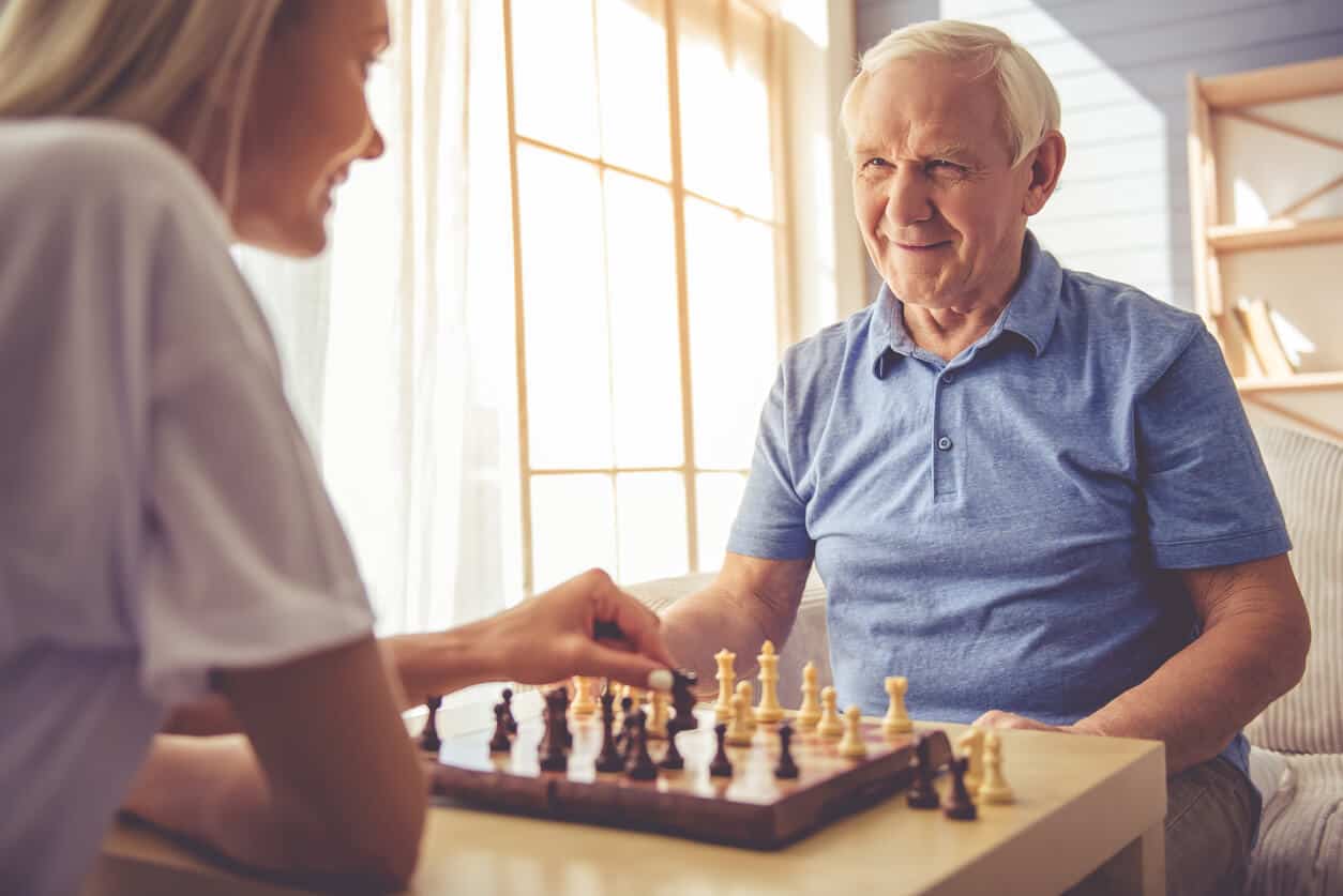 A live-in caregiver playing chess with a senior man in his home.