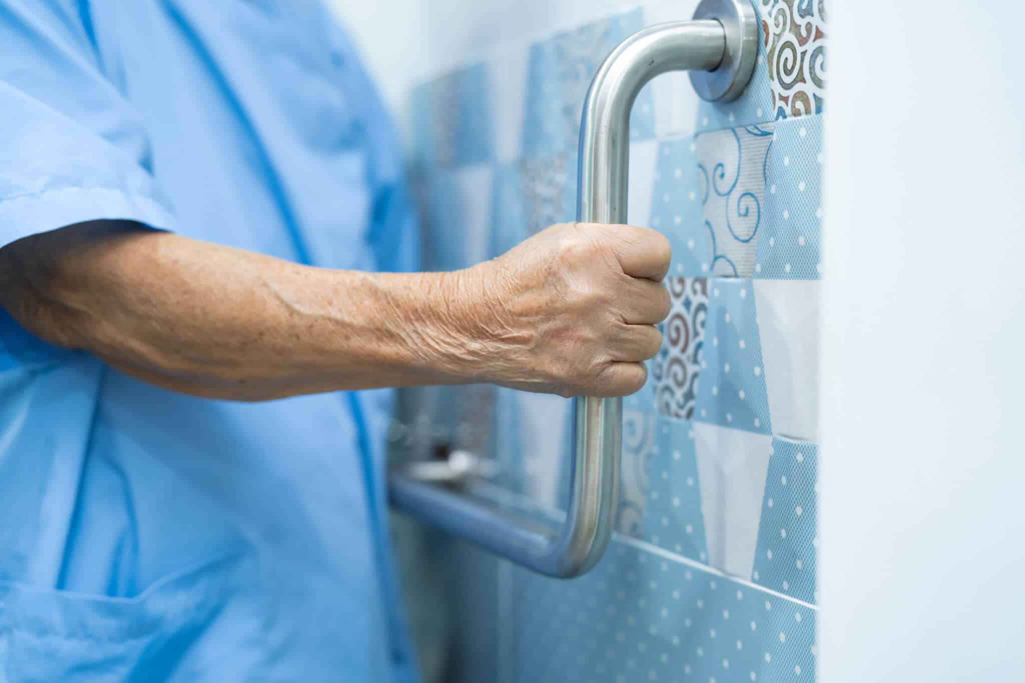 Senior woman using a toilet bathroom handle to help her stand steadily