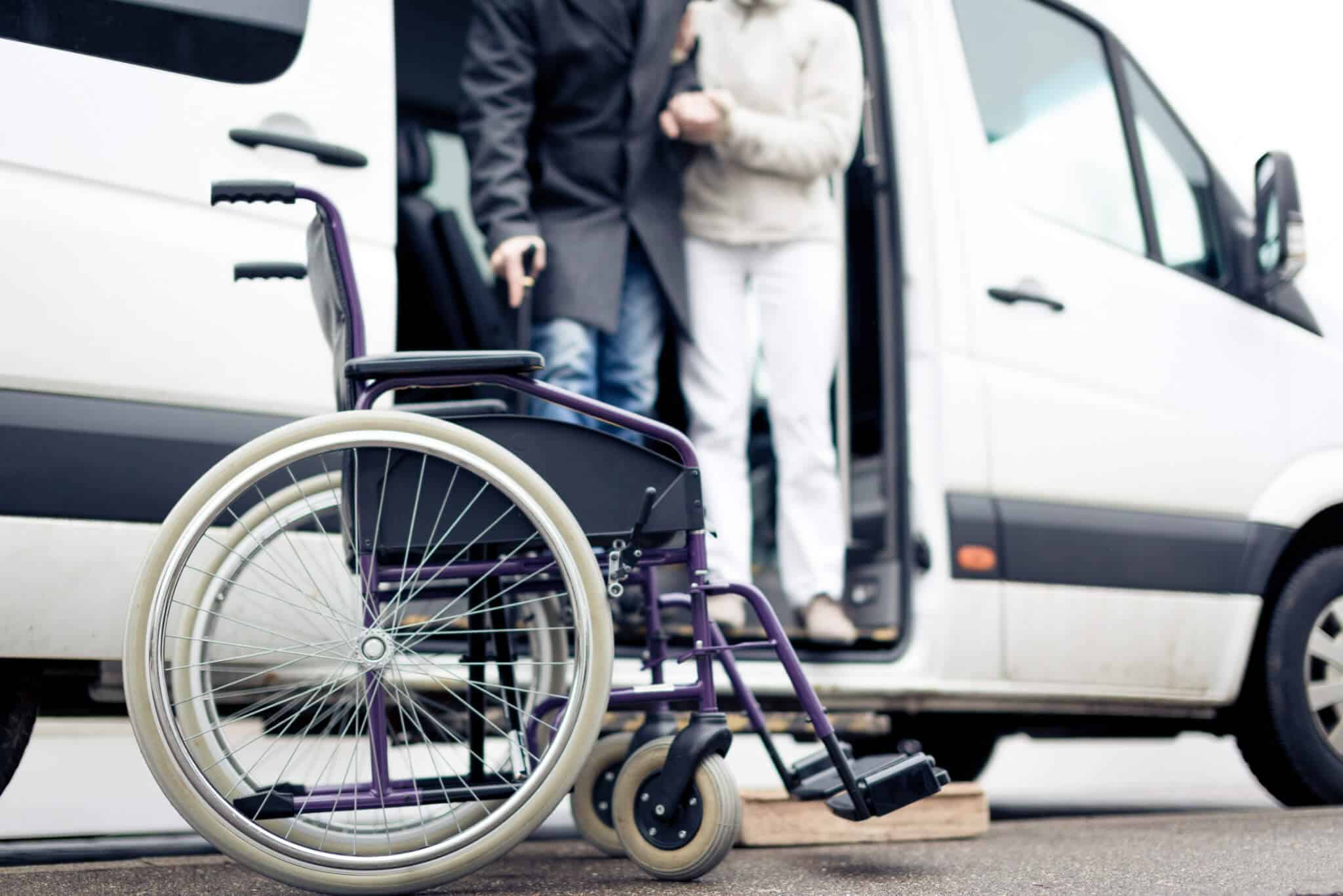 Caregiver helps senior man exit van into a wheelchair for an appointment