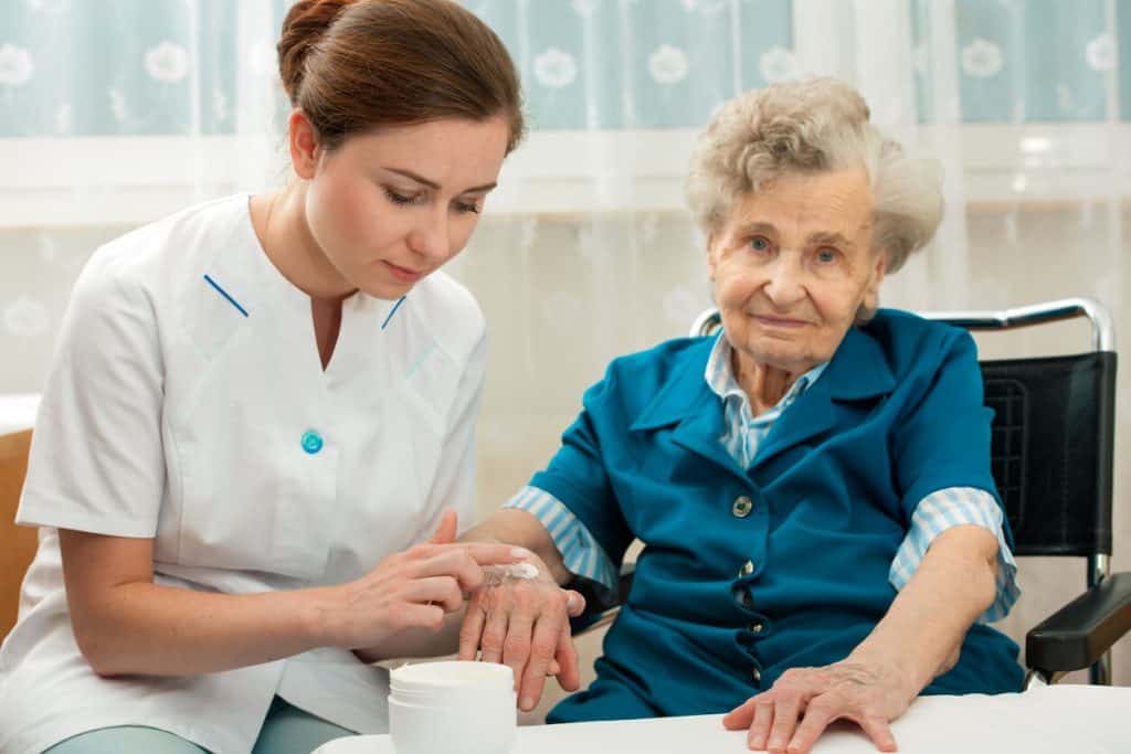 Female caregiver applying moisturizer on the hand of an elderly woman