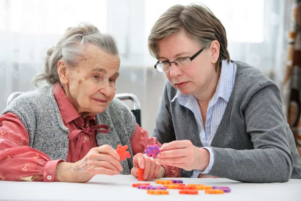 Senior woman with dementia putting together a puzzle with her caregiver: assisted living mental health.
