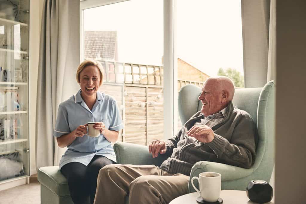 Senior man and female carer enjoying coffee at home. Private home caregiver jobs.