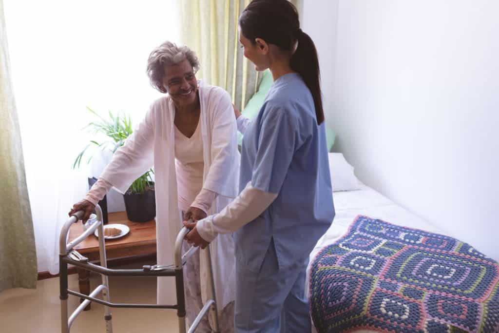A caregiver, performing senior caregiver jobs, is helping a female patient stand