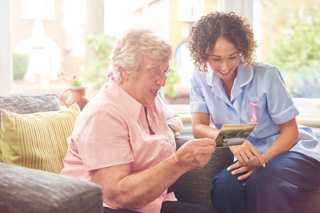 A caregiver in a enjoying quality time with an older woman as she shows her a postcard from her family: home care for seniors jobs
