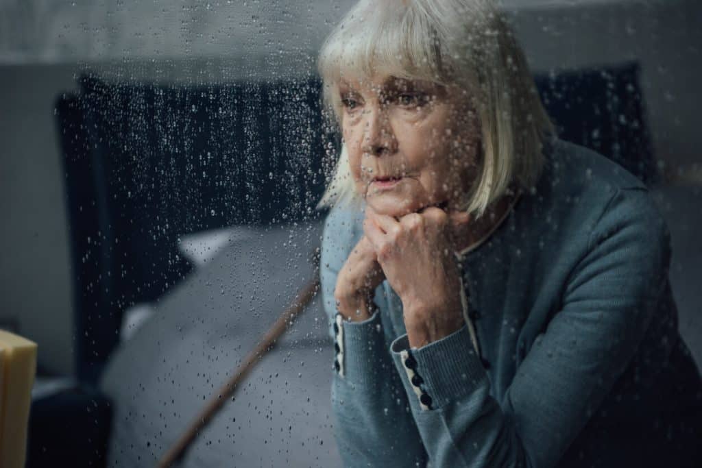Senior woman staring sadly out the window at the rain, jobs taking care of elderly