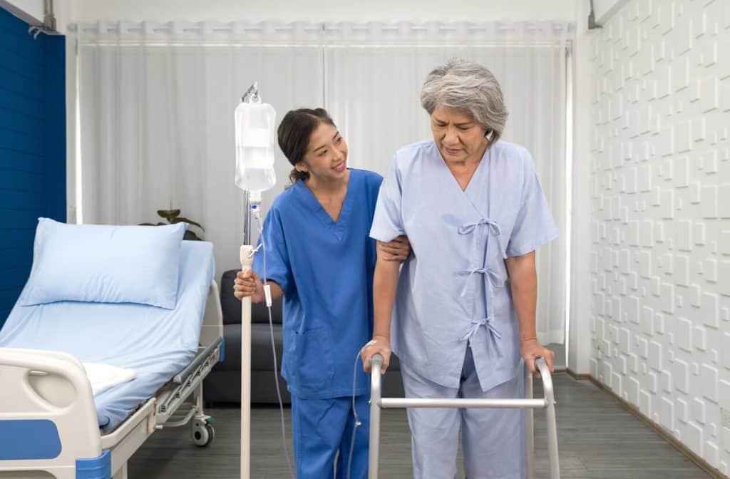 Home health care services nurse carrying IV and helping senior woman to walk with walker