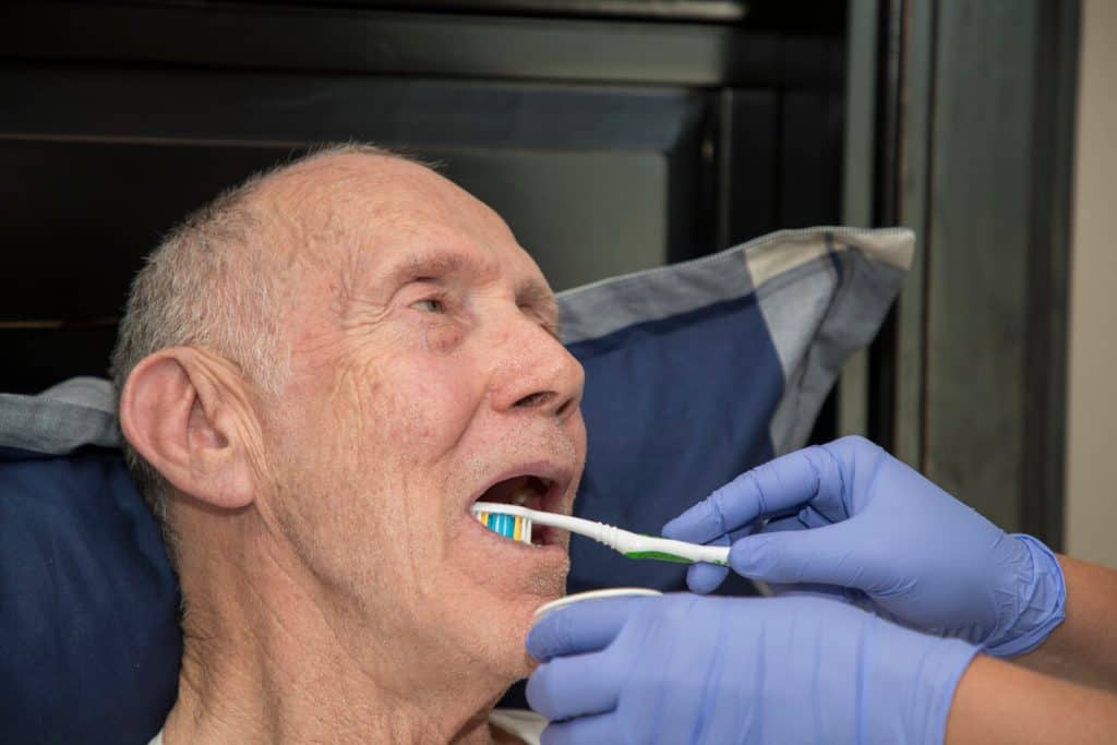Home health care services provider brushing the teeth of an elderly hospice patient