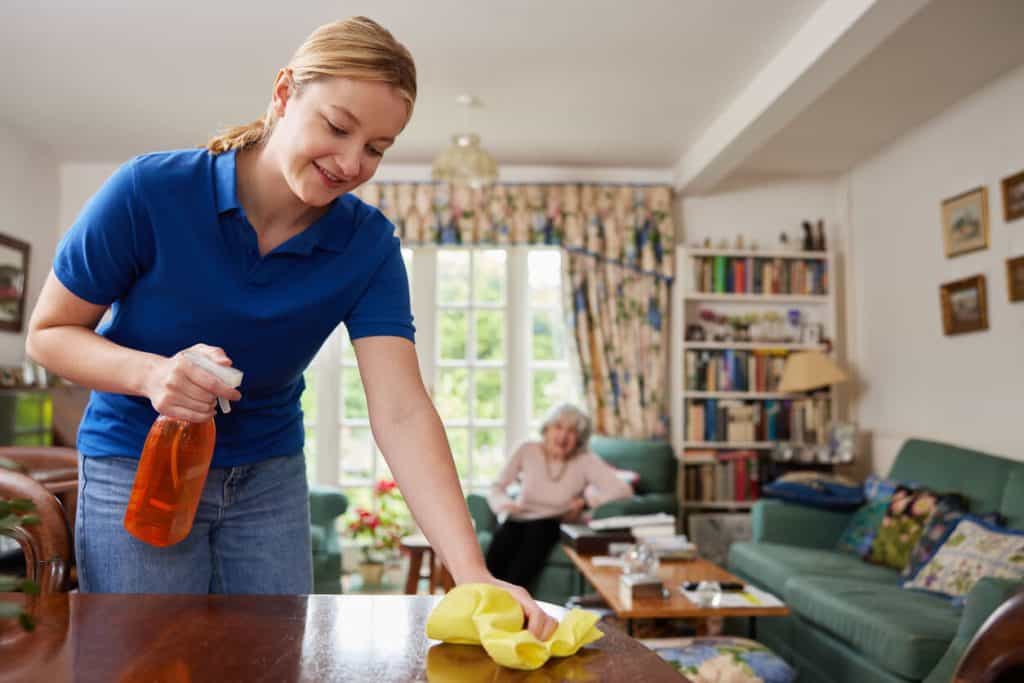 Female in-home elder caregiver assisting with housekeeping, and talking to an elderly woman