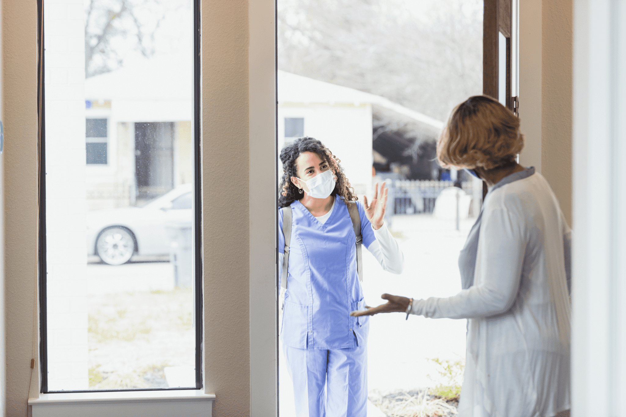 An elderly woman is welcoming a female home nurse into her home, home care nursing