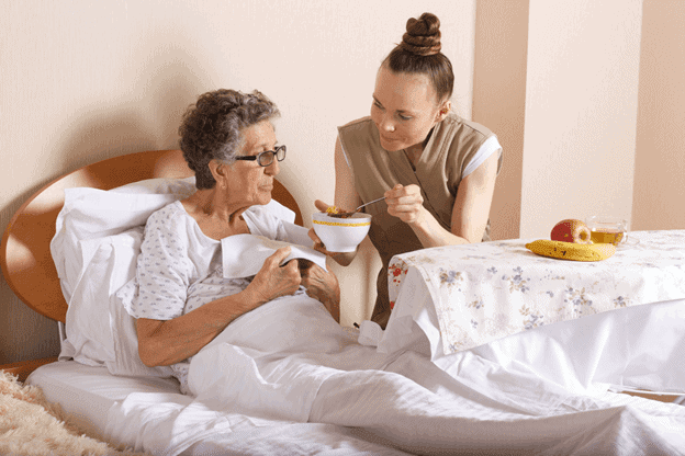 in-home care giver feeds an elderly woman at home, assisted living at home
