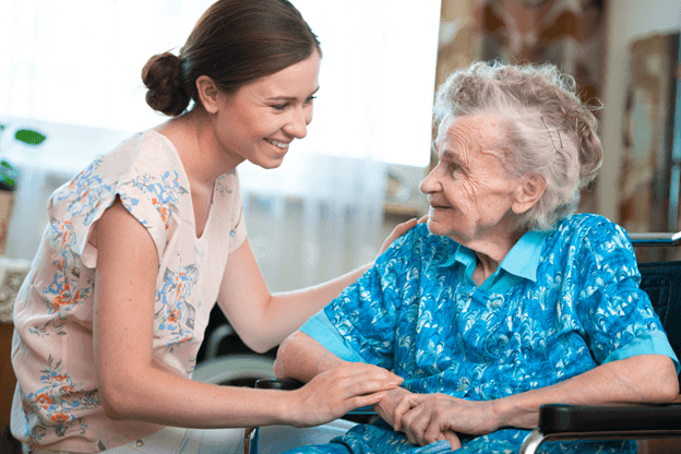 A female caregiver and an elderly woman smiling at each other, in home nursing care