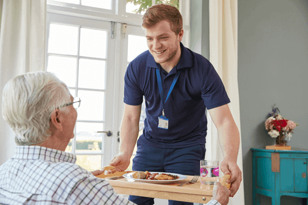 A male care provider serving dinner to an elderly man through in home nursing