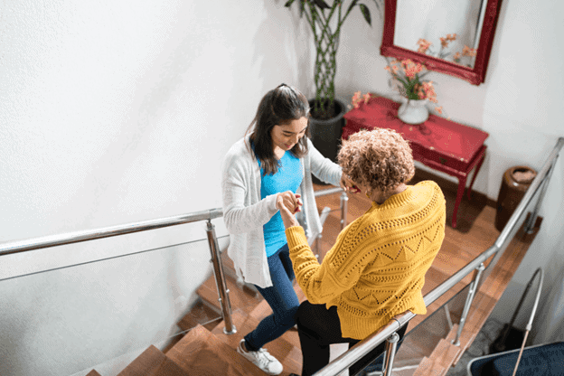 A female caregiver helping elderly woman move up stairs in home nursing