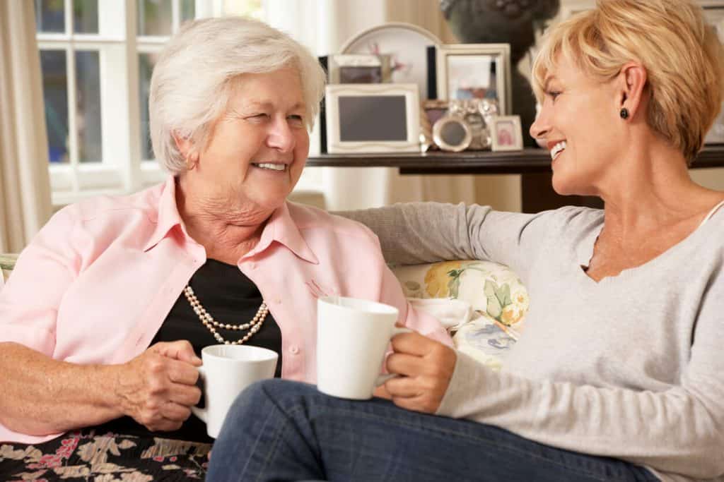 Mature daughter and senior mother sitting on a couch smiling and talking best care, assistance home care