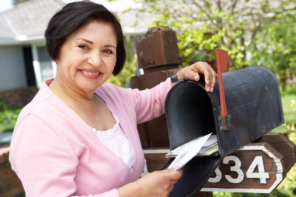 Senior woman happily getting her penpal letter out of the mailbox during covid, elderly pen pal