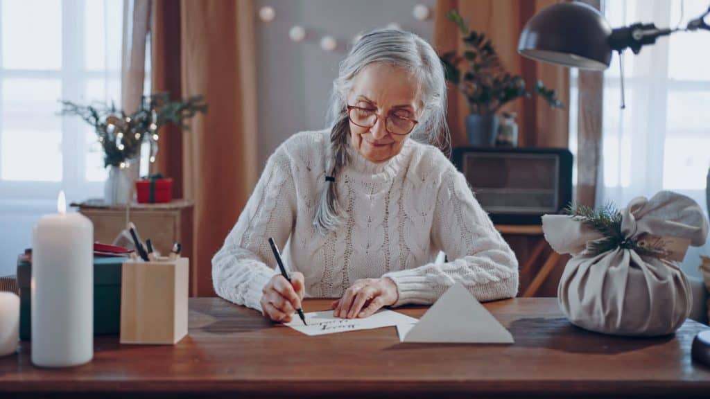 Senior woman with white braid writing a letter to her penpal, elderly pen pal