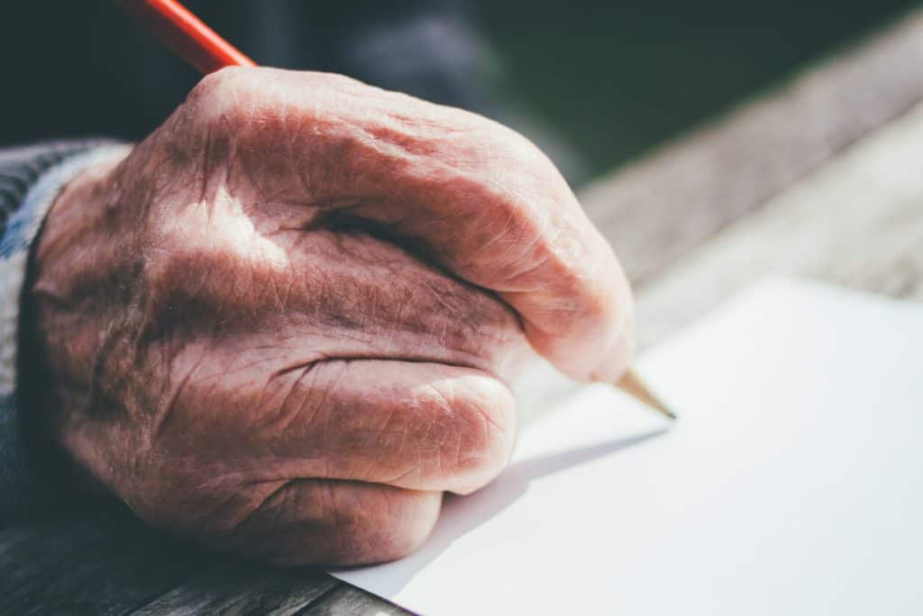 Elderly man holding a pencil poised to write a letter to his penpal , elderly pen pal