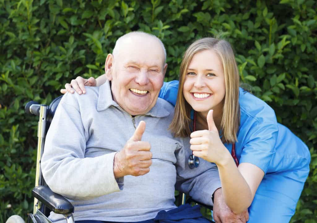 senior man in a wheelchair giving thumbs up with his elder care sitter. jobs sitting with the elderly