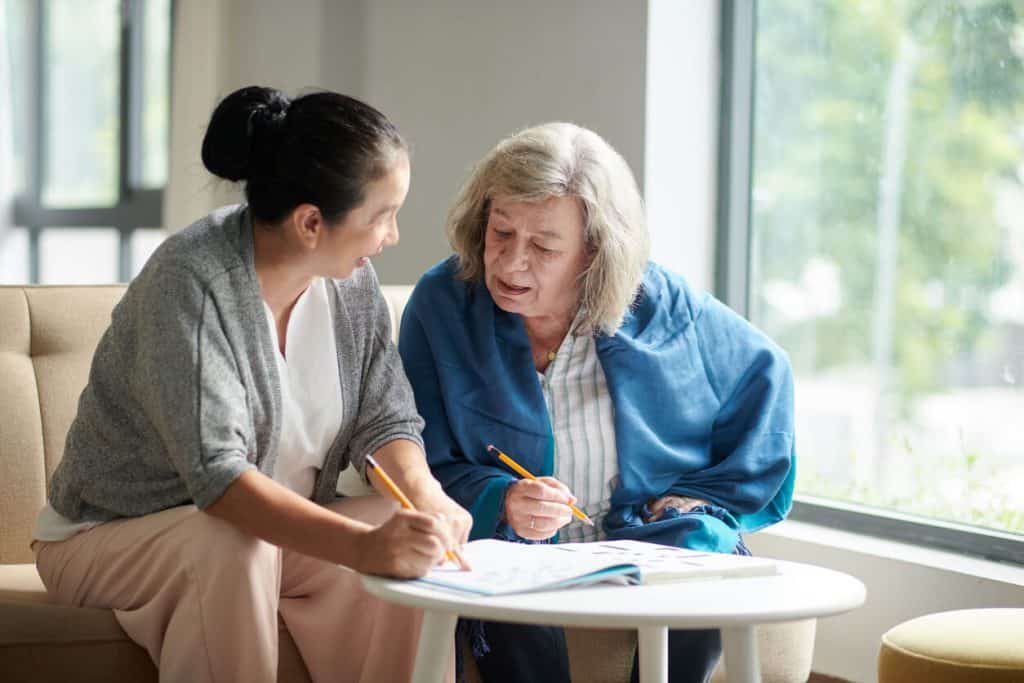 caregiver and senior woman doing a crossword puzzle together. sitters for the elderly jobs