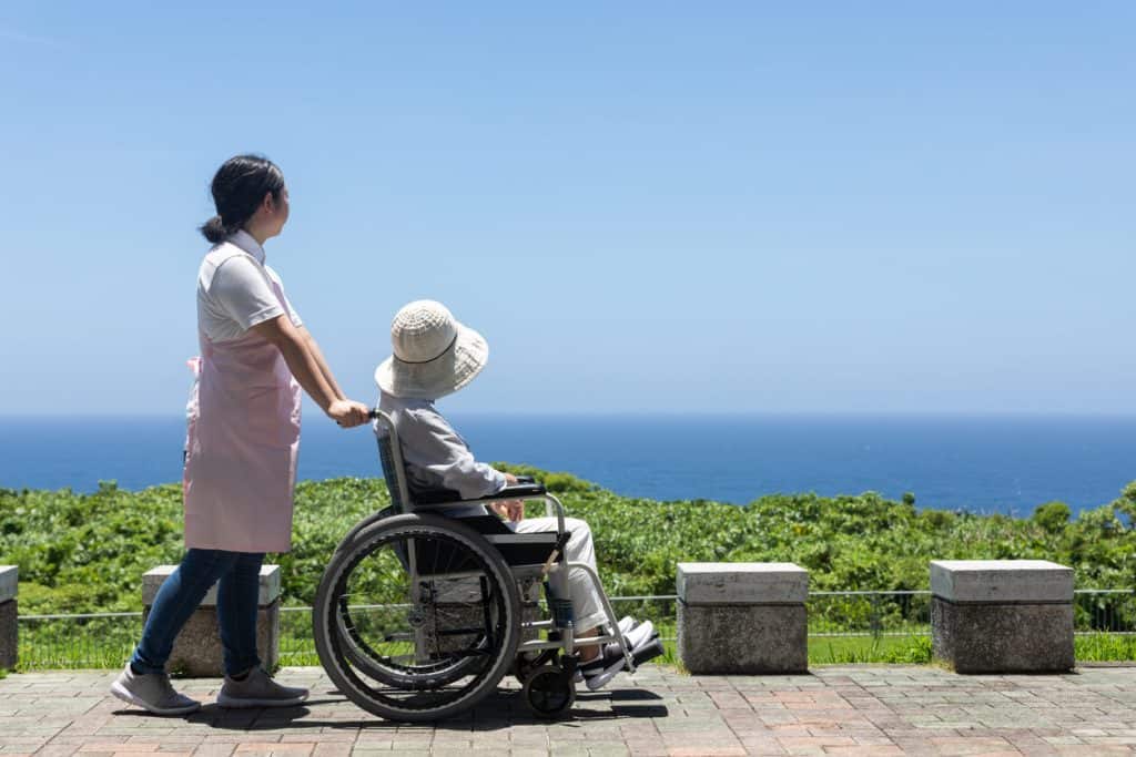 caregiver pushing elderly woman outside in her wheelchair. sitters for the elderly jobs