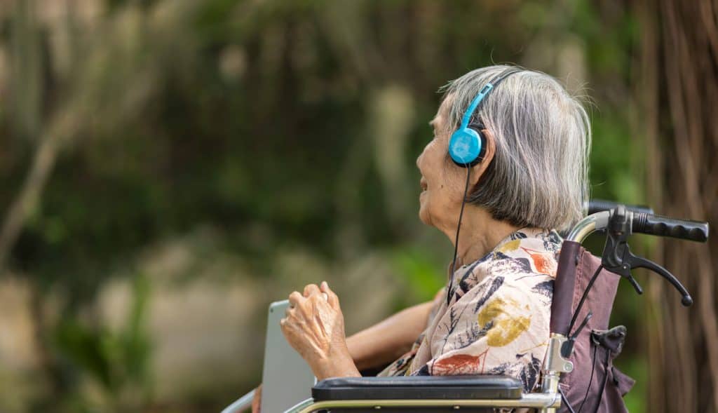 elderly woman with dementia in wheelchair listening to music with headphones. sitters for the elderly jobs