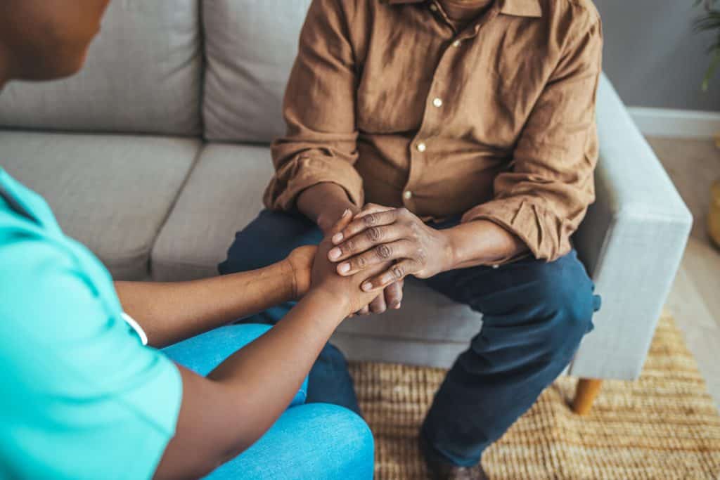 compassionate caregiver holding a senior man’s hand at home, become a caregiver
