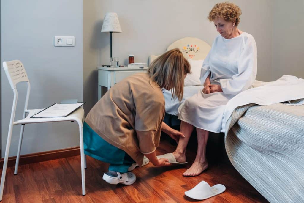 Personal Care Assistant helping older woman wear her slipper - caregiver classes