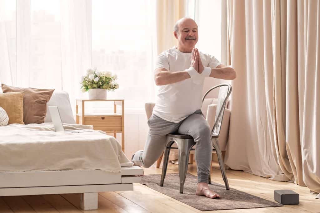 An elderly man doing chair yoga in his bedroom. unique activities for seniors