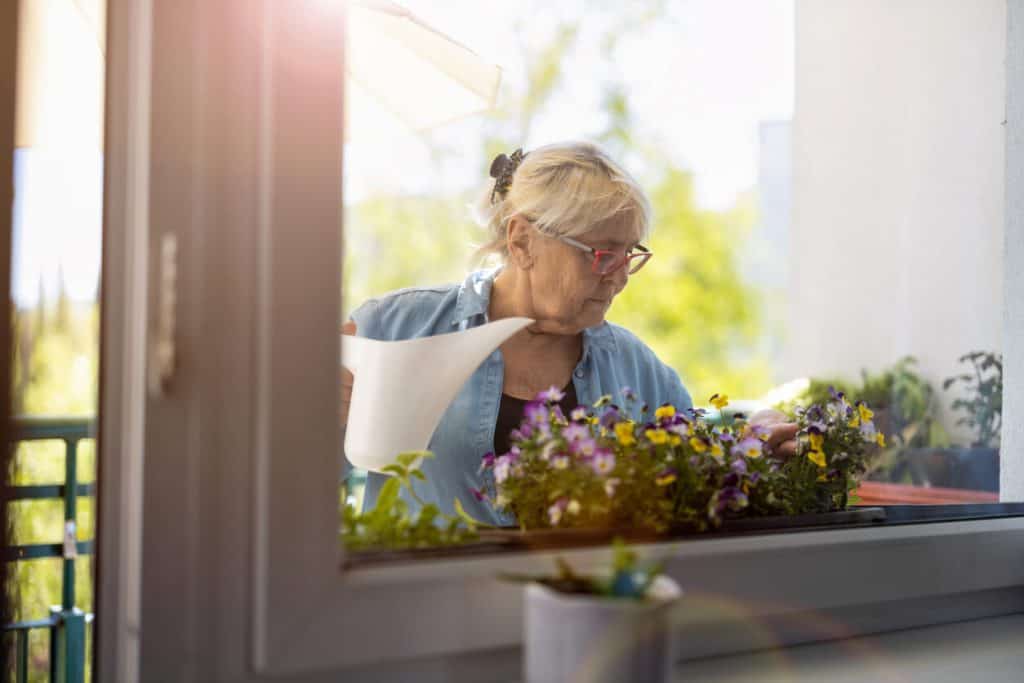 A senior woman watering the plants on her balcony. unique activities for seniors
