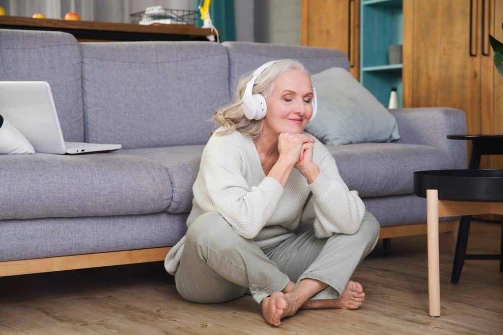 A smiling senior woman with headphones sitting on the floor. unique activities for seniors