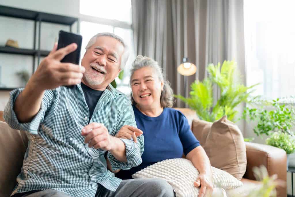 A happy senior couple sitting on a sofa using a phone to video call. unique activities for seniors