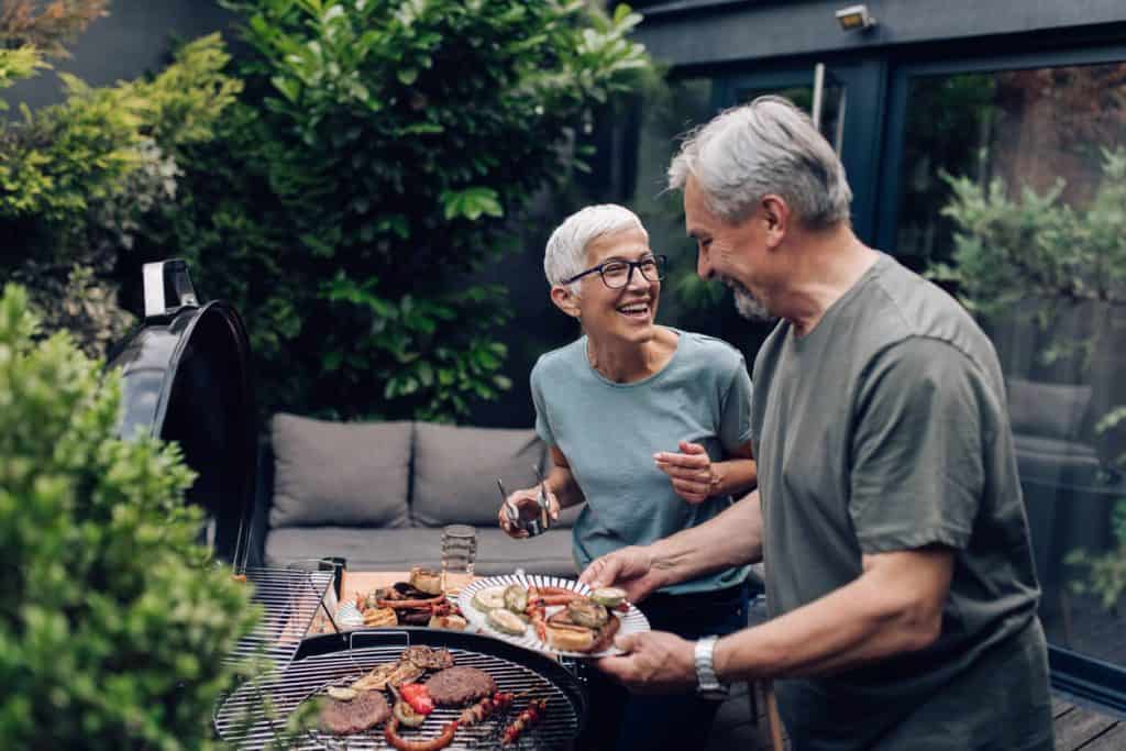 an elderly couple enjoying outdoor activities by grilling meat for their loved ones. outdoor activities for seniors