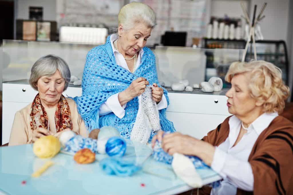 Three older women knitting in a retirement home, constructive activities for seniors in assisted living environments