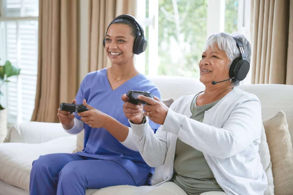 A senior and a caregiver playing video game, fun activities for seniors in assisted living homes 2022