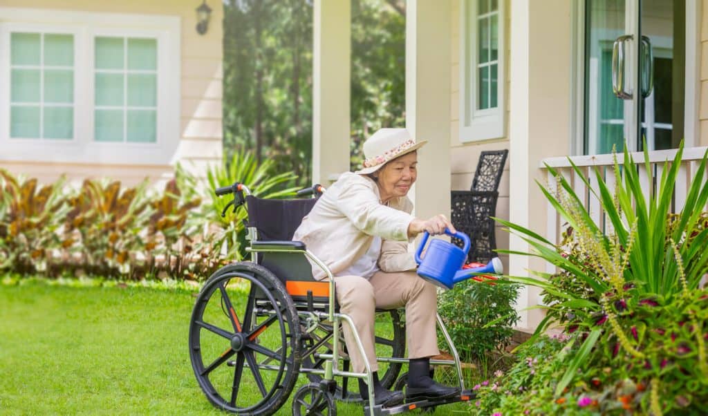 An older woman watering plants in the backyard of assisted living home, activities for seniors in elderly homes to keep them active