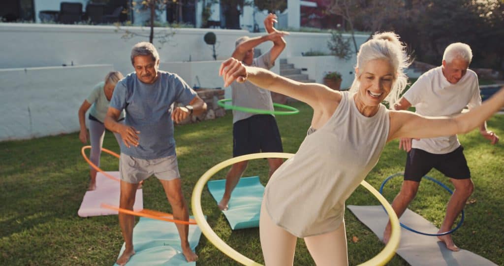 Older people working out with hoola hoops outdoors, outdoor activities for seniors in nursing home