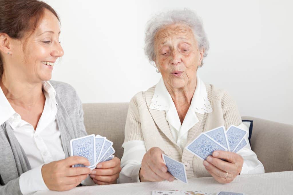 Caregiver with a senior woman playing cards as a home activity for seniors