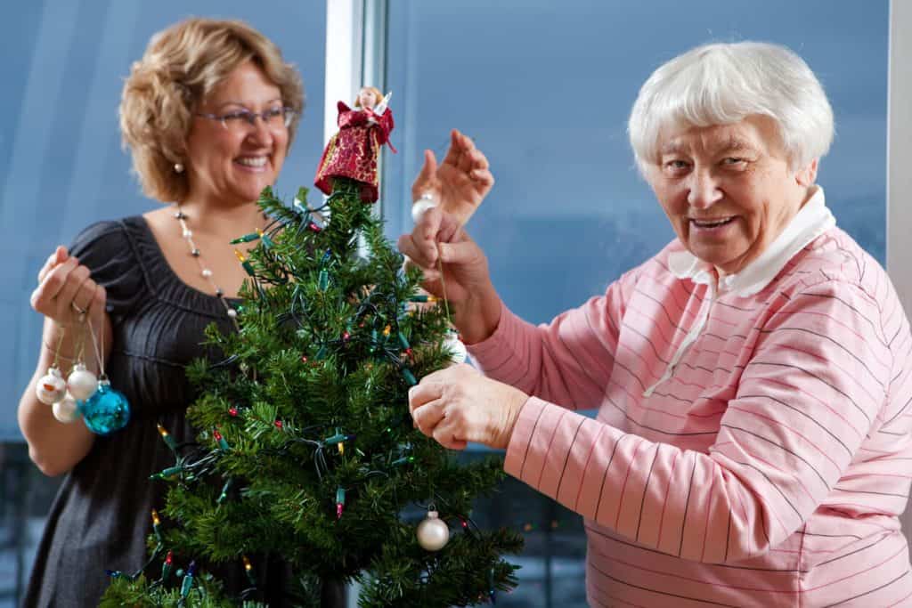Caregiver helping senior woman decorate her Christmas tree, activities for seniors in December