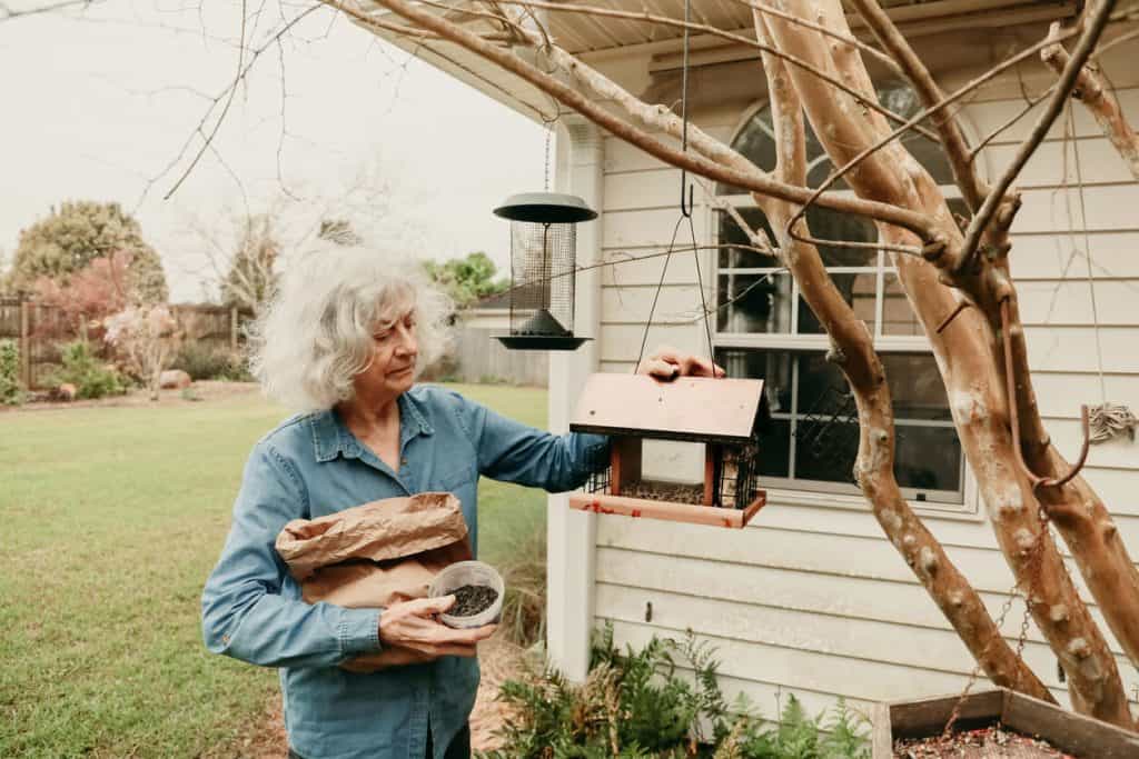 Mature senior woman filling a bird feeder with seed, one on one activities for seniors with dementia