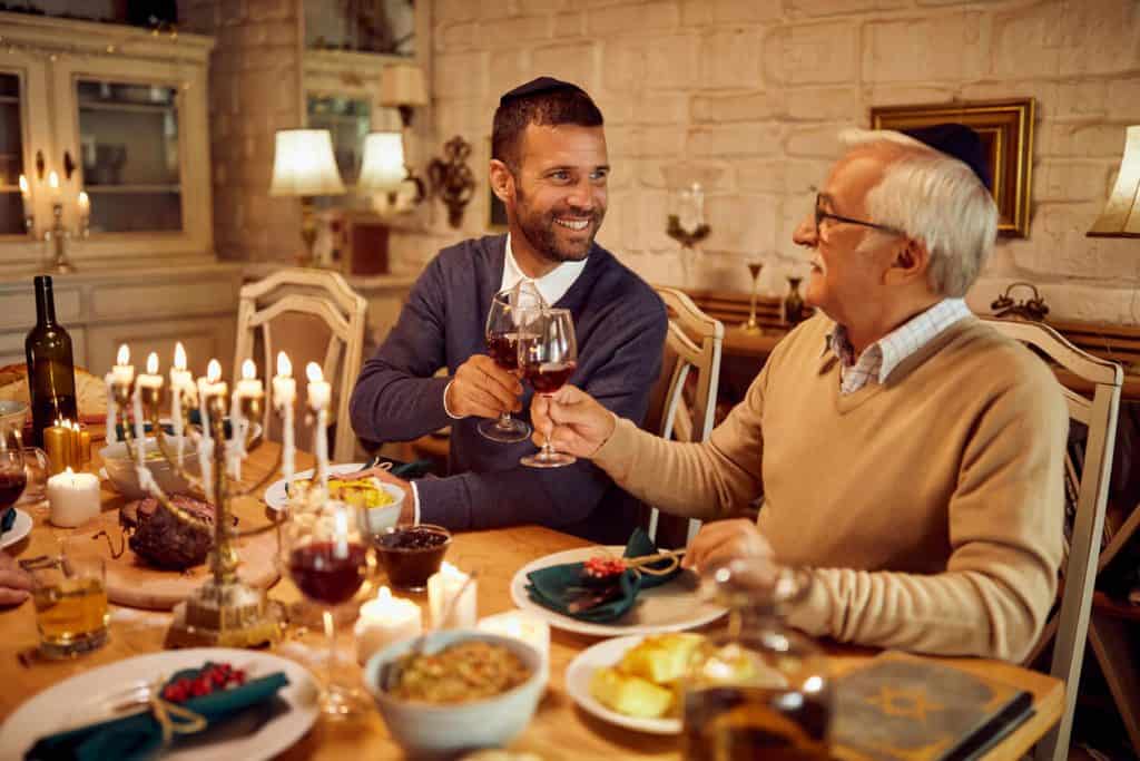 Jewish senior man celebrating Hanukkah with a family member, great traditional foods, and a menorah. 2022 assisted living menus