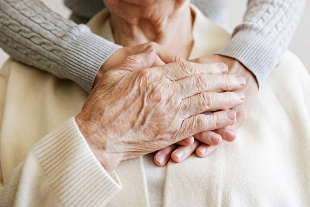 a caregiver holding an older woman’s hands, questions to ask for assisted living
