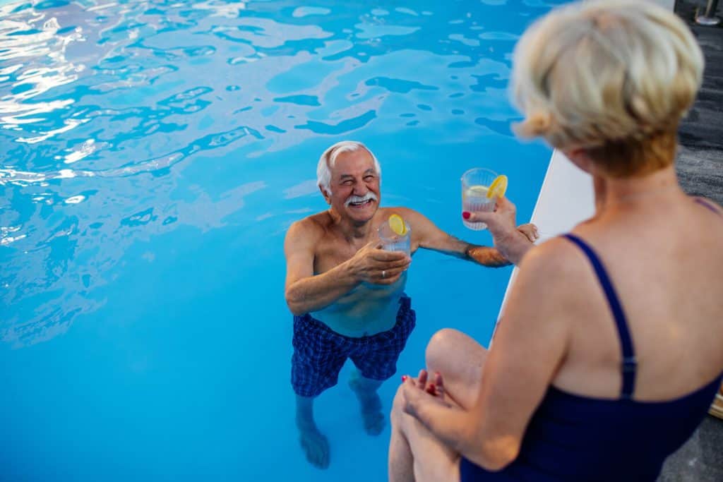 Senior man and woman poolside toasting with a glass of lemonade and enjoying privacy, luxurious assisted living